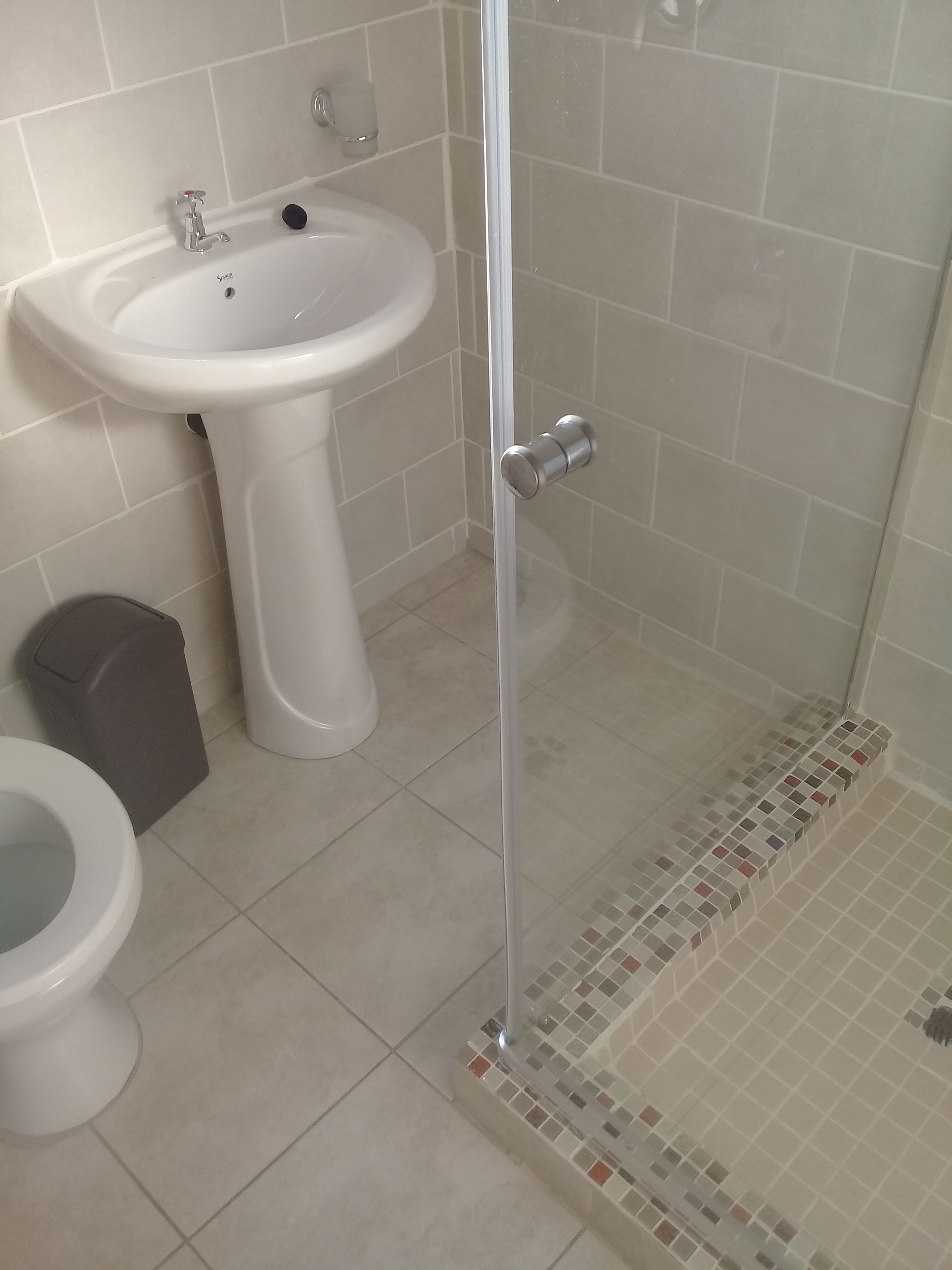 A bathroom with a white pedestal sink, a toilet, and a glass shower enclosure.