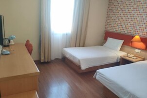Una habitación de hotel con dos camas, un escritorio con lámpara y una ventana con cortinas.