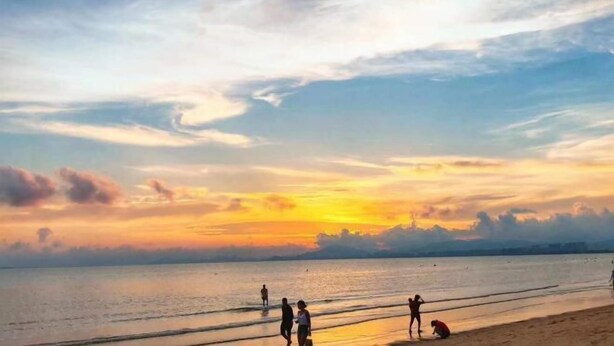 Una spiaggia al tramonto con persone che camminano e giocano in acqua.