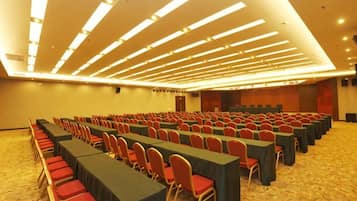 Un salón de conferencias con filas de mesas y sillas, un escenario y suelo alfombrado.