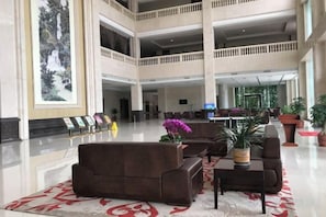 Un hall d’entrée spacieux, doté de plusieurs espaces de détente, d’un comptoir d’accueil et d’une grande œuvre d’art accrochée au mur.