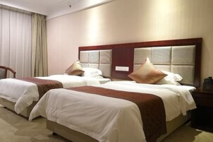 Habitación de hotel con dos camas, cada una con cabecero de madera y ropa de cama blanca.