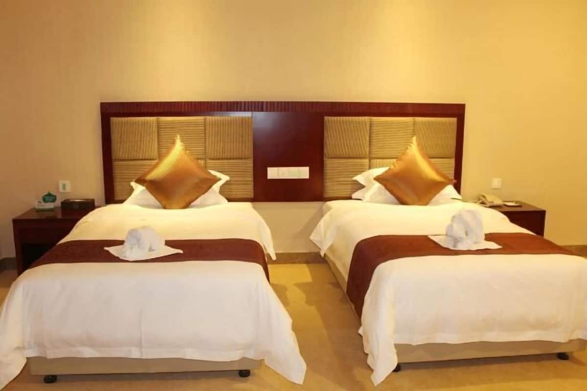 Una habitación de hotel con dos camas, cabecero de madera y una mesita de noche con lámpara.