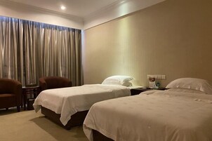 Habitación de hotel con dos camas individuales, un escritorio, una silla y un ventanal con cortinas.