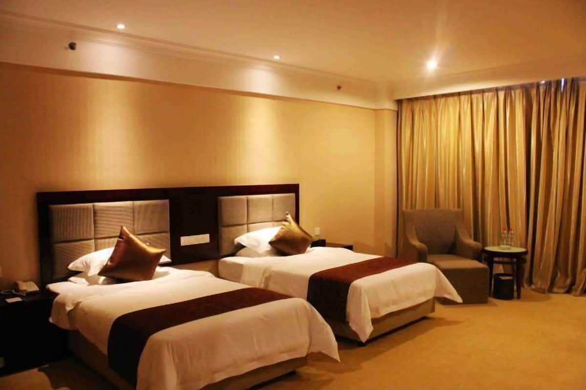 Habitación de hotel con dos camas, una silla, una mesita y una cortina.