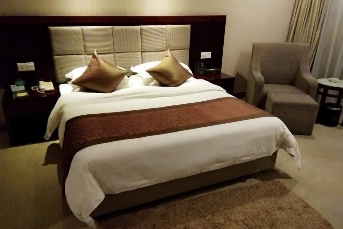 Una habitación de hotel con una cama grande, una mesita de noche con un teléfono y una lámpara, una silla y una pequeña mesa.