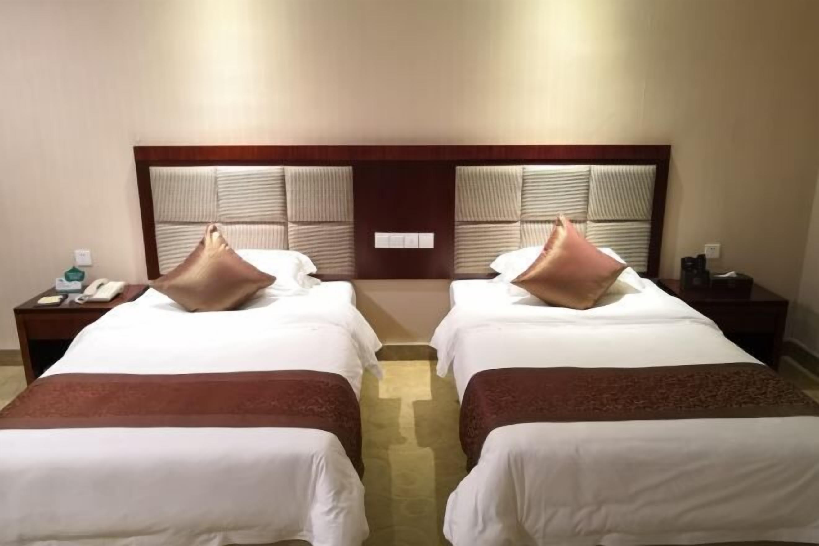 A hotel room with two beds, each with a pillow and a bedside table with a phone and a lamp.