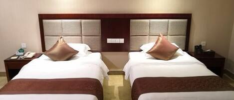 A hotel room with two beds, each with a pillow and a bedside table with a phone and a lamp.