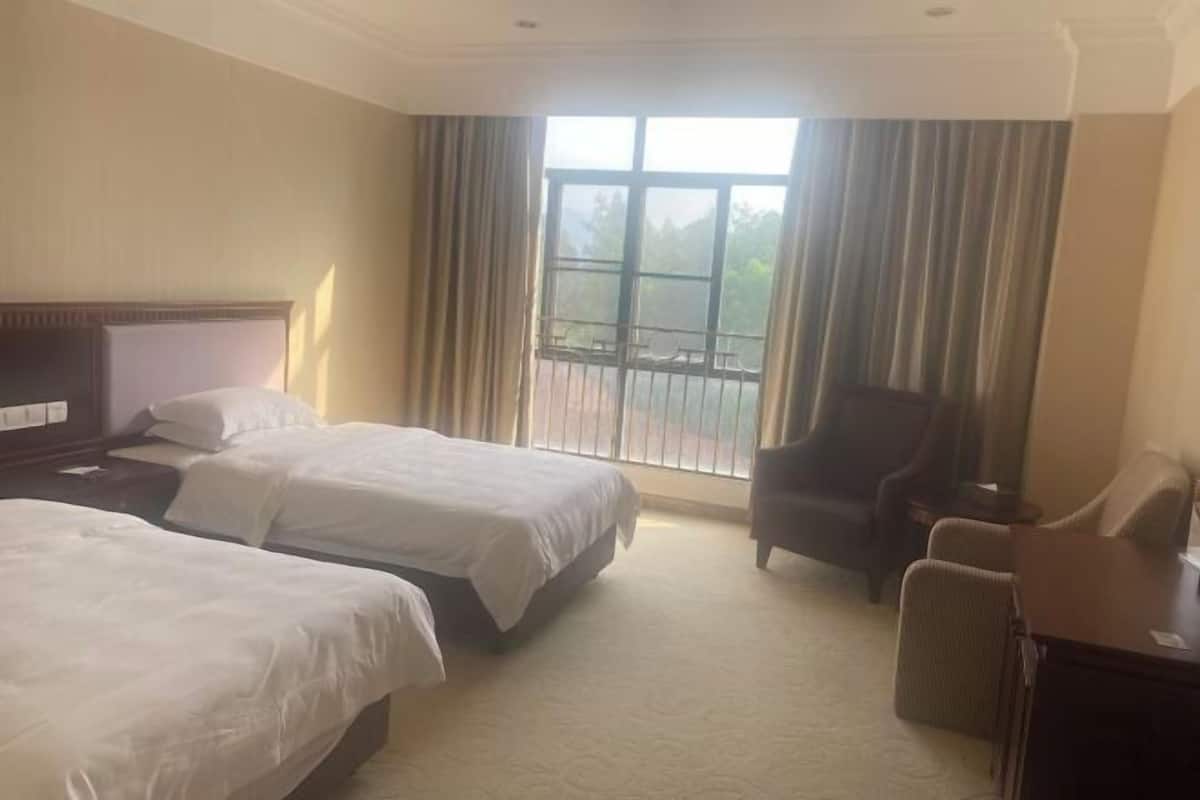 Habitación de hotel con dos camas, una silla, un escritorio y un amplio ventanal con cortinas.