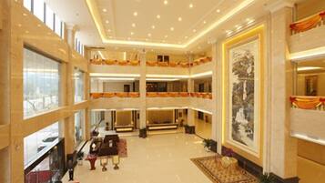 Un hall de hotel de varios niveles con una imponente escalera, un mostrador de recepción y una gran obra de arte enmarcada en la pared.