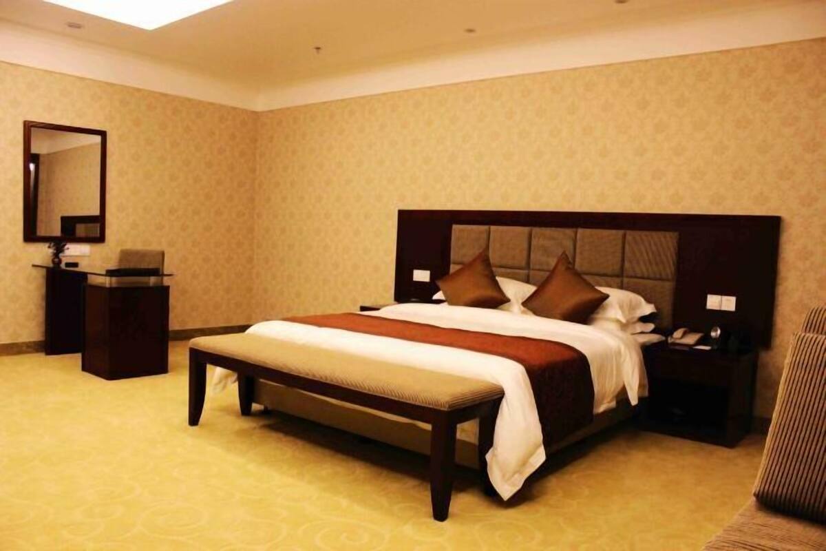 Una habitación de hotel con una cama grande, una mesita de noche, un banco y un espejo.