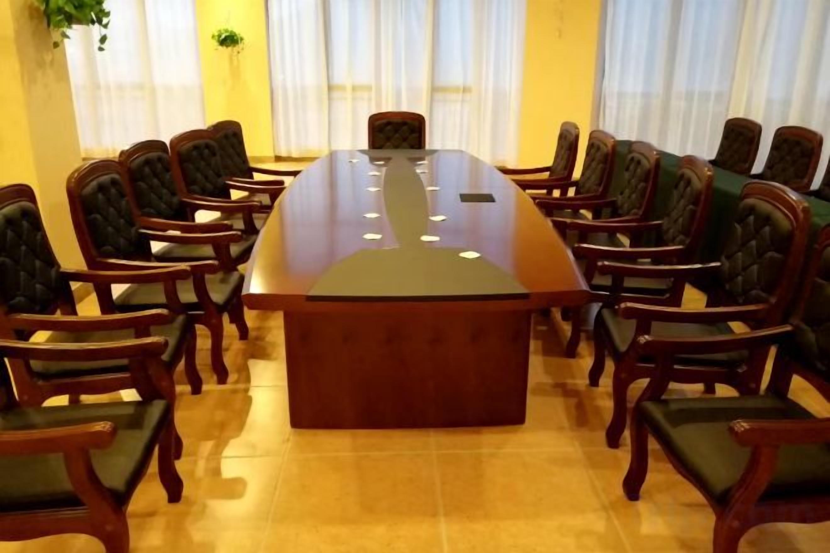 Un salón de conferencias con una gran mesa ovalada rodeada de sillas.