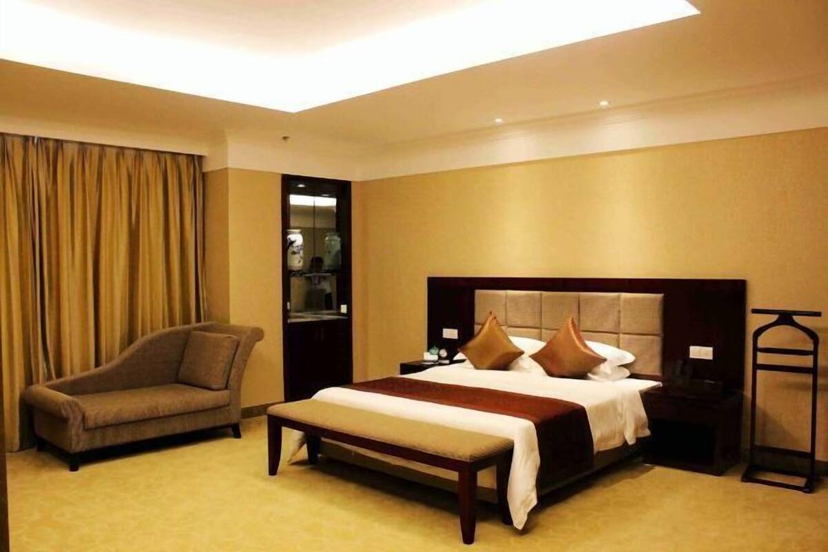 Una habitación de hotel con cama, banca, sillón, mesita de noche y armario.