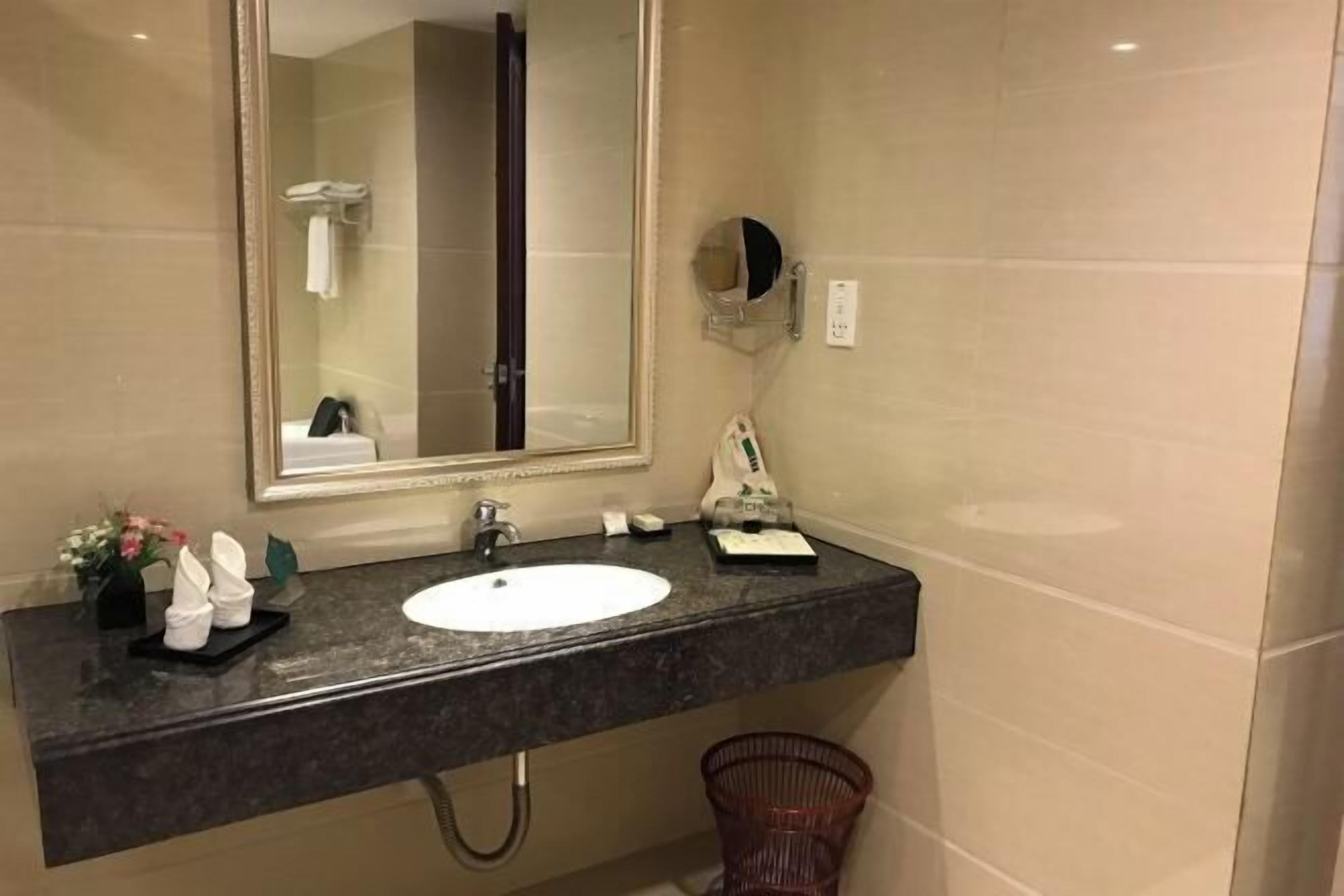 Un baño con lavamanos, espejo, toallero y cubo de basura.