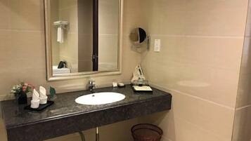 Un baño con lavamanos, espejo, toallero y cubo de basura.
