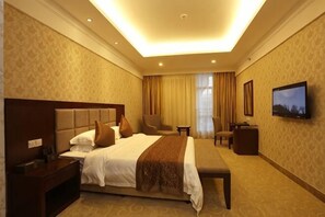 A hotel room with a large bed, a desk, a chair, a TV, and a window with curtains. - Uchoice Hotel (Jiexi)