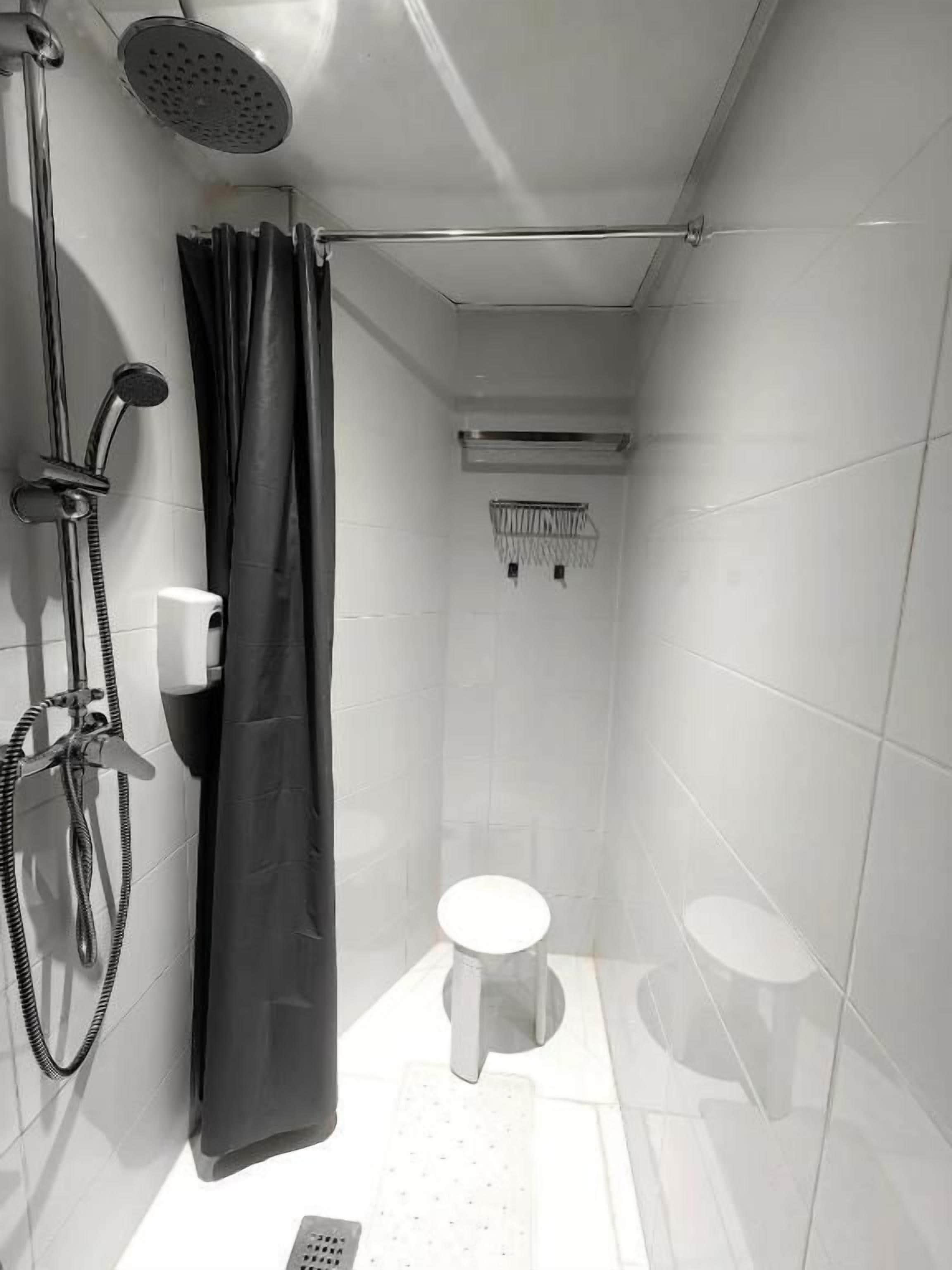 A small, tiled bathroom with a shower, toilet, and a towel rack.