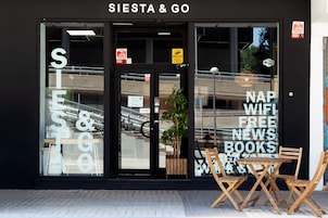 Ein Schaufenster mit der Aufschrift 'SIESTA & GO' und einem Schild, das kostenloses WLAN, Nachrichten und Bücher anbietet.