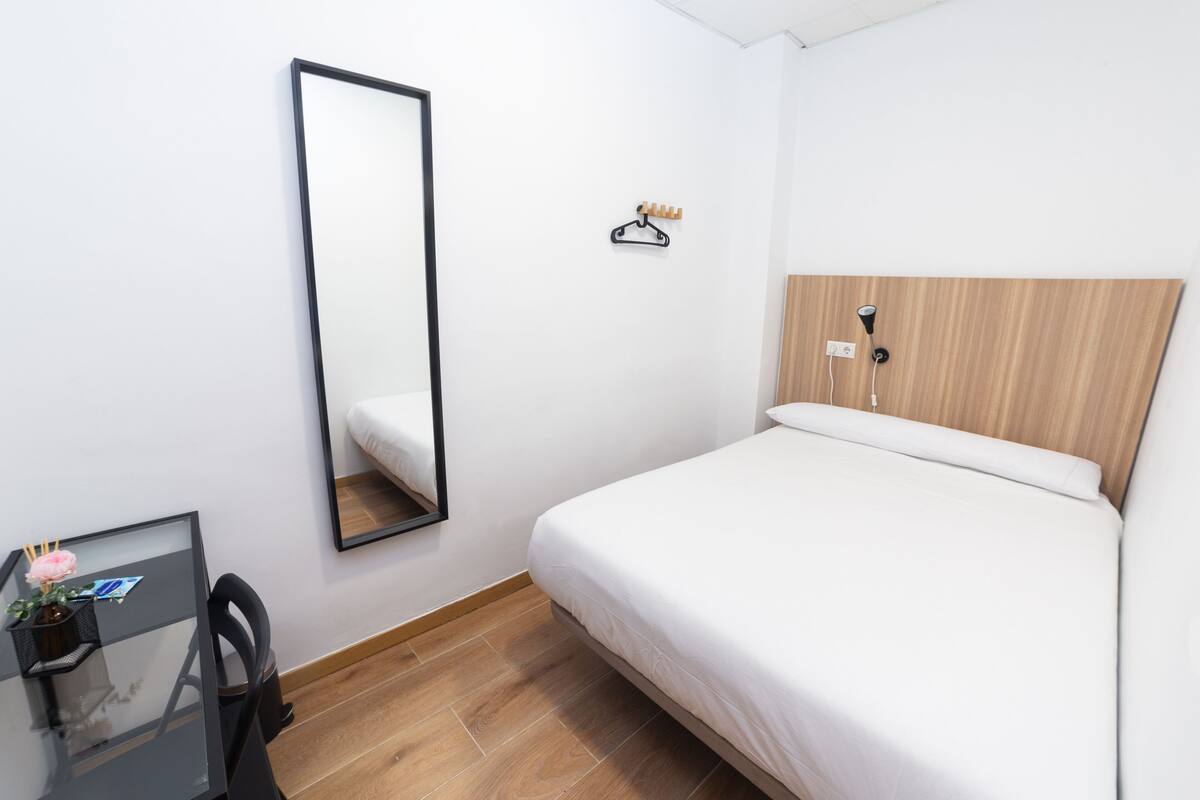 Una habitación de hotel con una cama, un escritorio con silla, un espejo y un cabecero de madera.