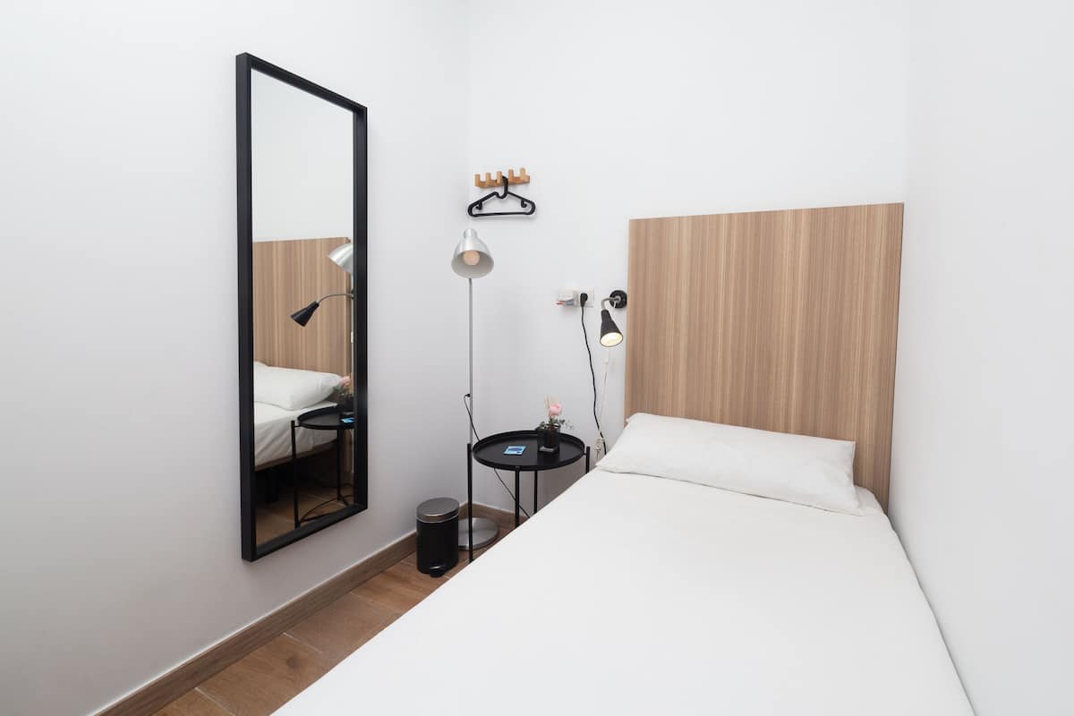 Una habitación de hotel moderna con cabecera de madera, un espejo grande, una mesita de noche con lámpara y una pequeña mesa redonda con lámpara.