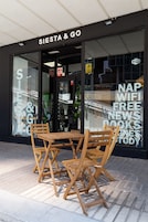 Ein Geschäft mit einer Schaufensterreklame mit dem Schriftzug "SIESTA & GO" und einem Tisch mit Stühlen vor der Tür.