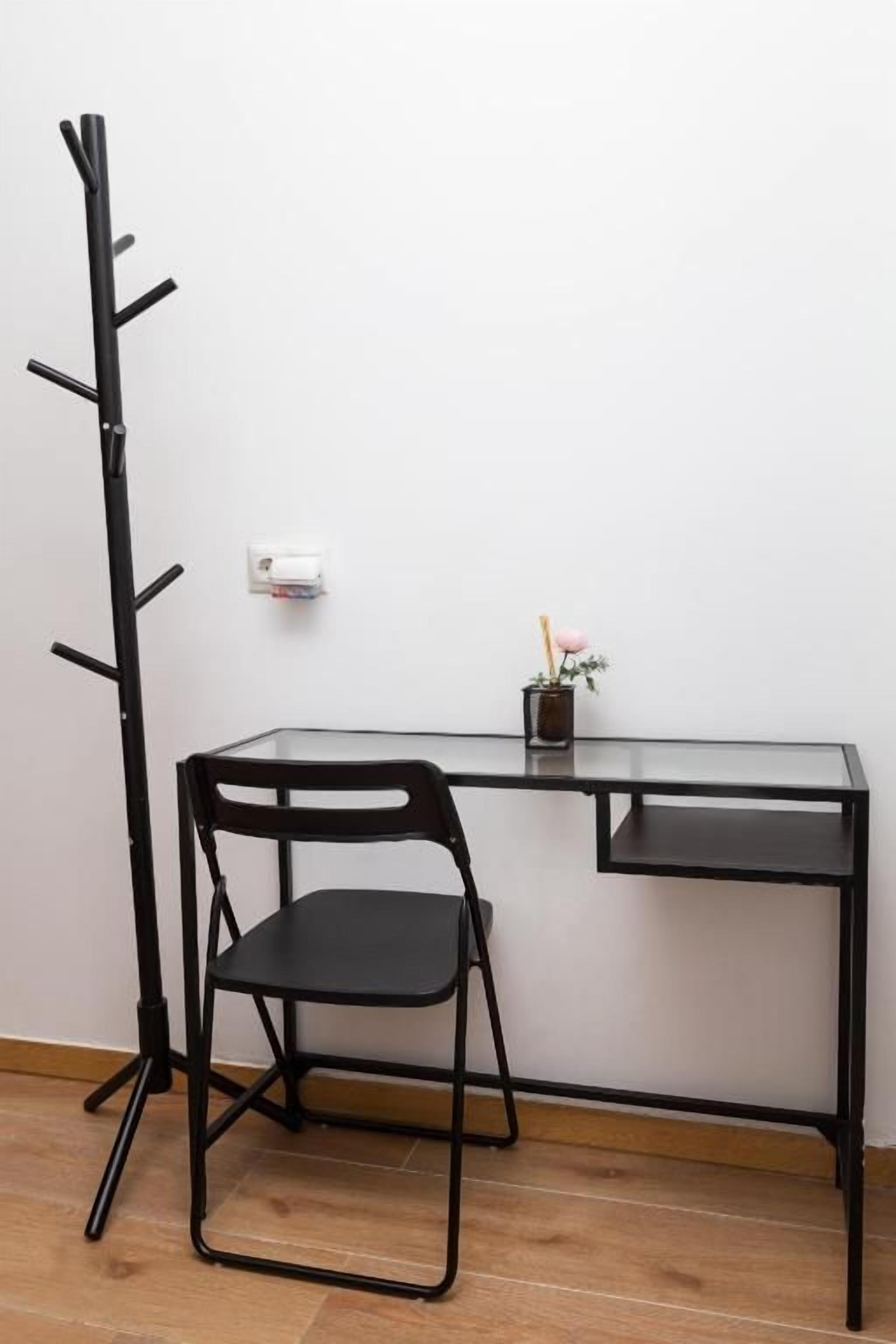 A room with a black metal desk, a black metal chair, and a black metal coat rack.