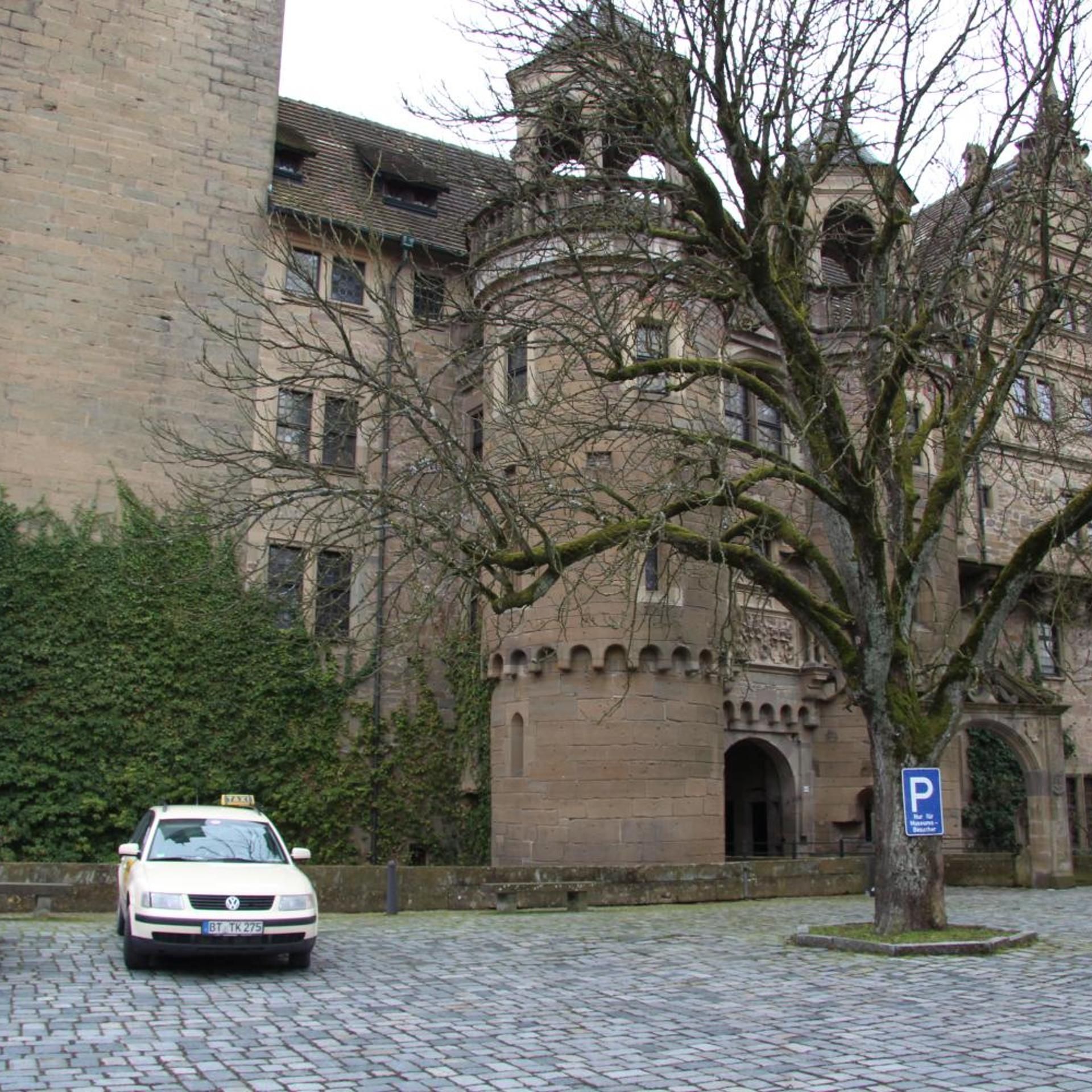 Un taxi blanco estacionado frente a un edificio histórico con un árbol en primer plano.