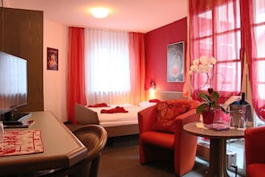 A hotel room with a bed, a desk, a chair, a table, and a window with curtains.