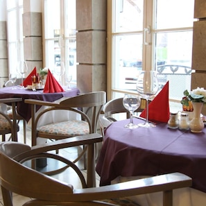 A restaurant interior with tables set for dining, chairs, and a view through large windows.