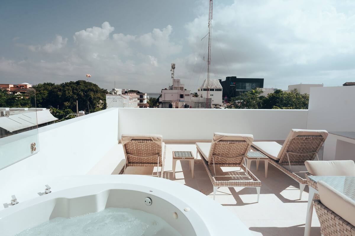 A rooftop terrace with a hot tub, lounge chairs, and a view of the cityscape.