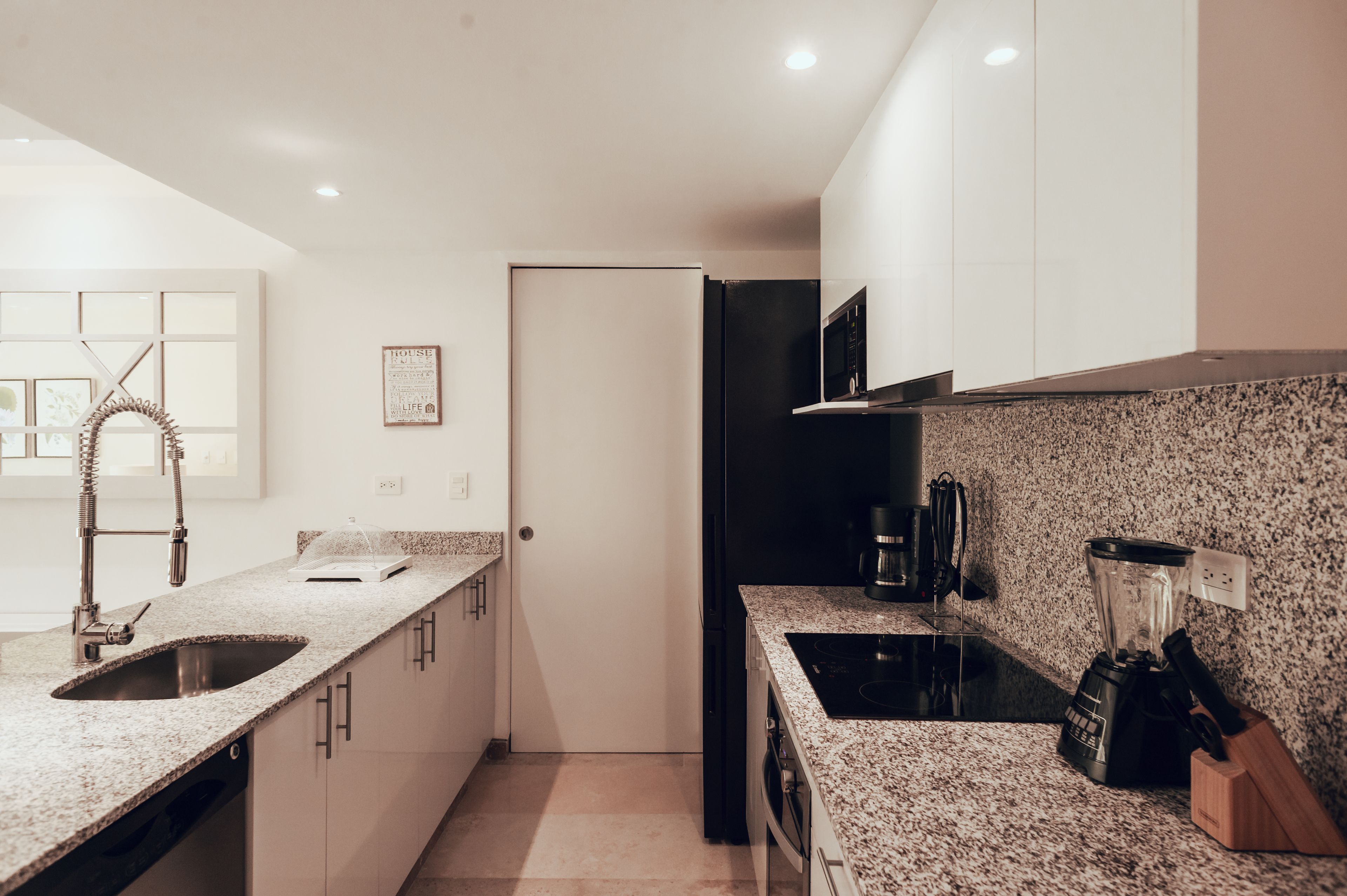 A modern kitchen with granite countertops, a black refrigerator, a built-in oven, and a blender on the counter.
