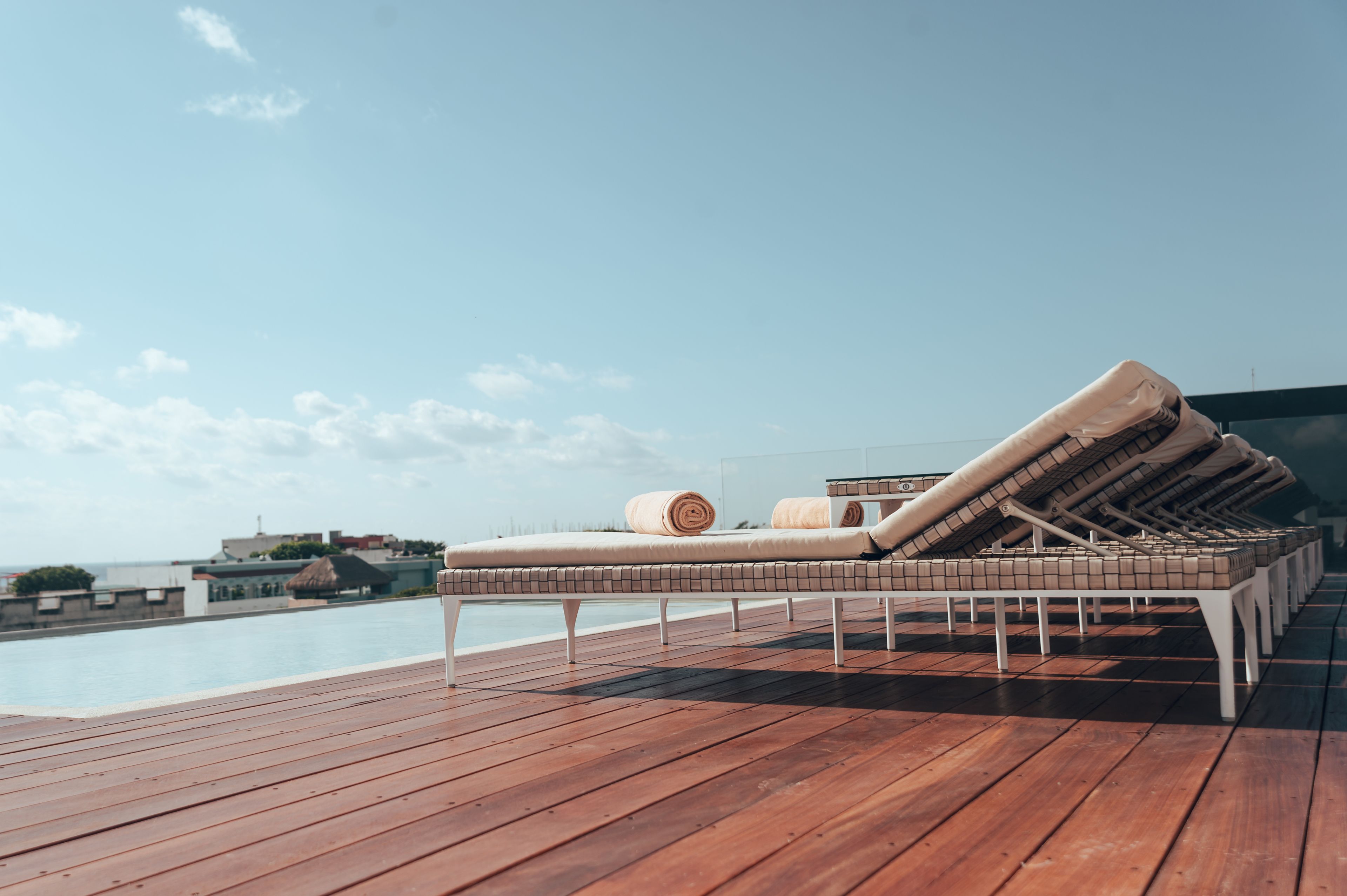 A wooden deck with a poolside lounge area featuring sun loungers and towels.