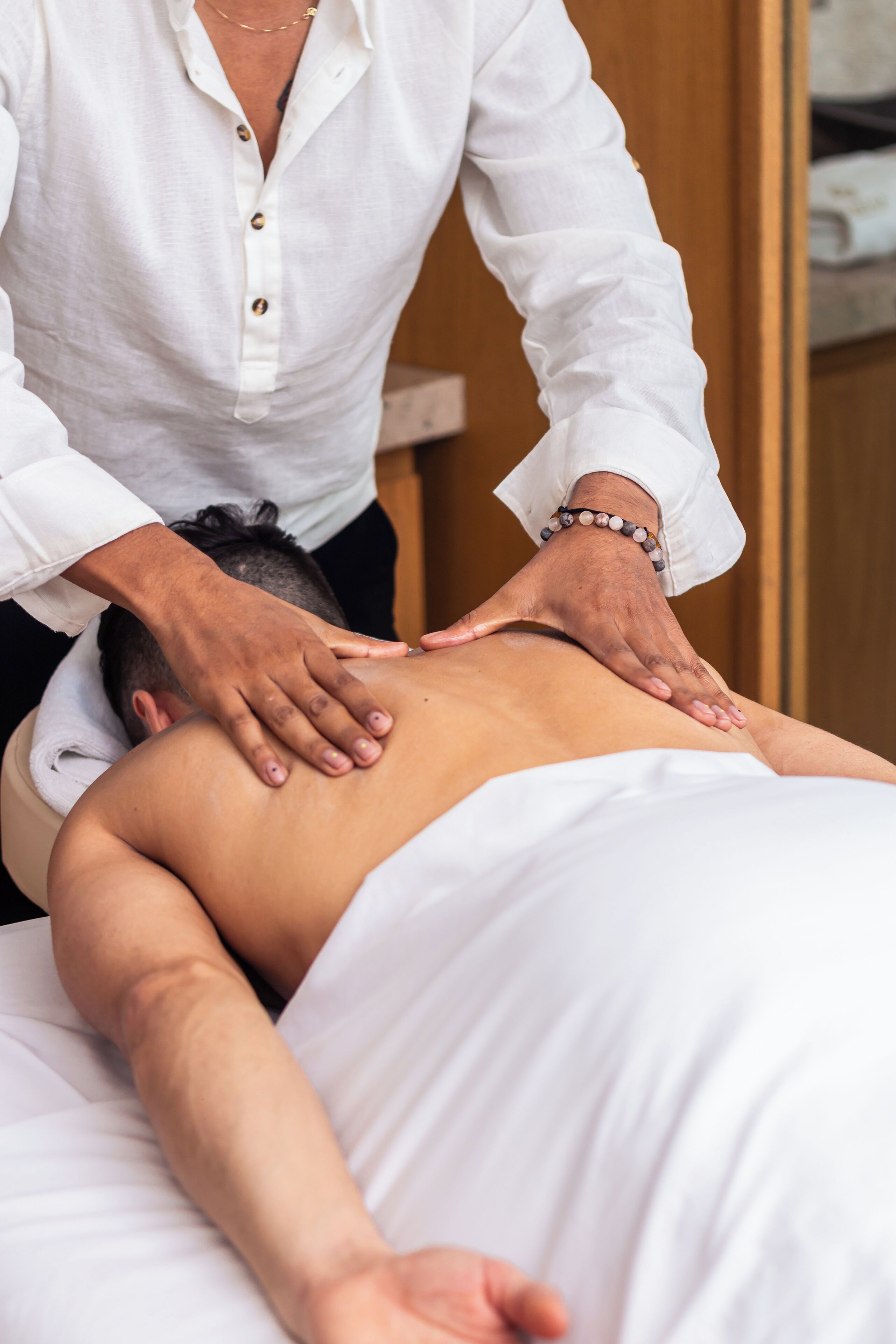 A person receiving a back massage in a room with wooden furniture and a white wall.