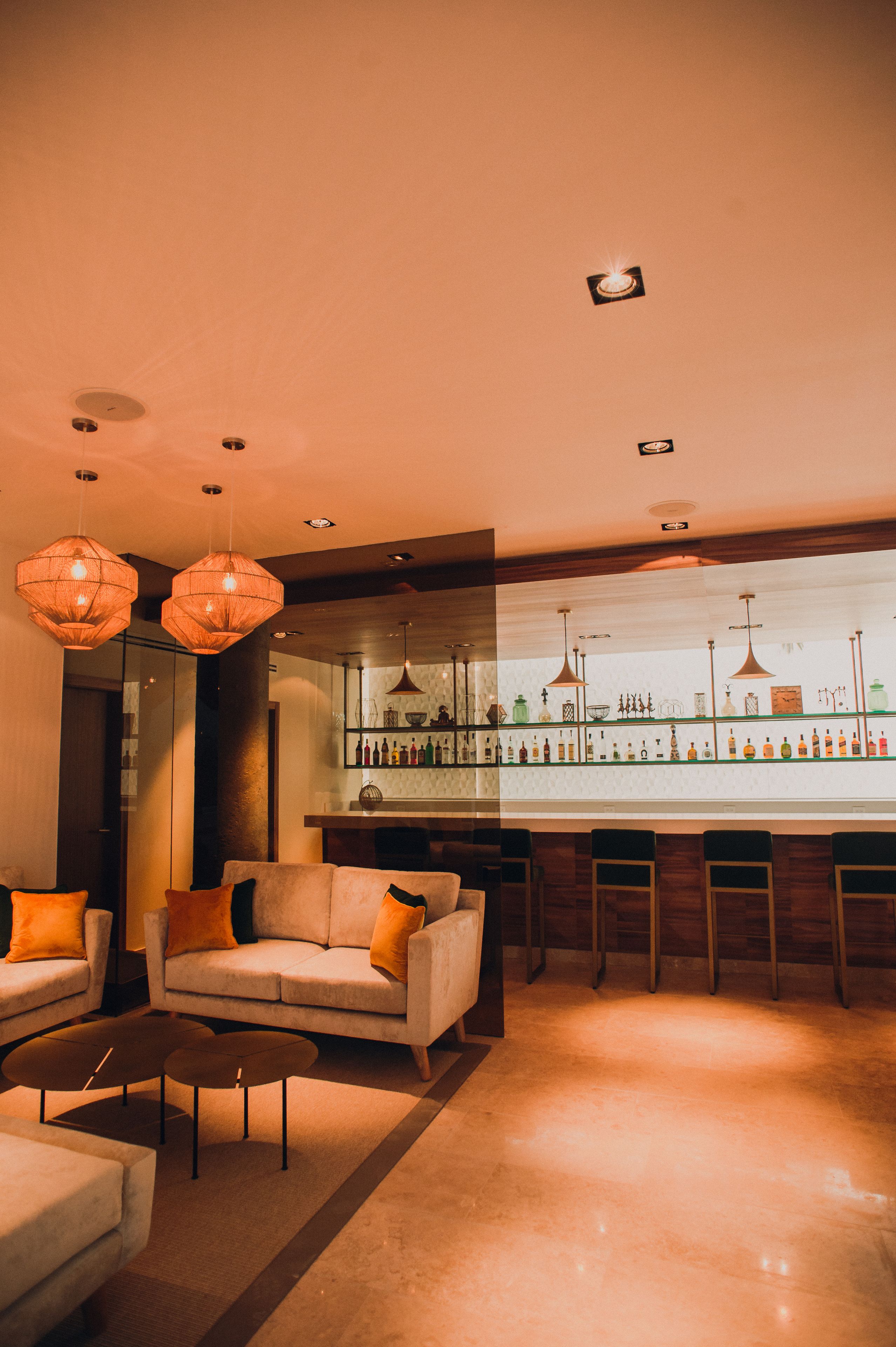 Una zona de bar con una barra larga, varias luces colgantes y un espacio de estar con sofás y sillones.
