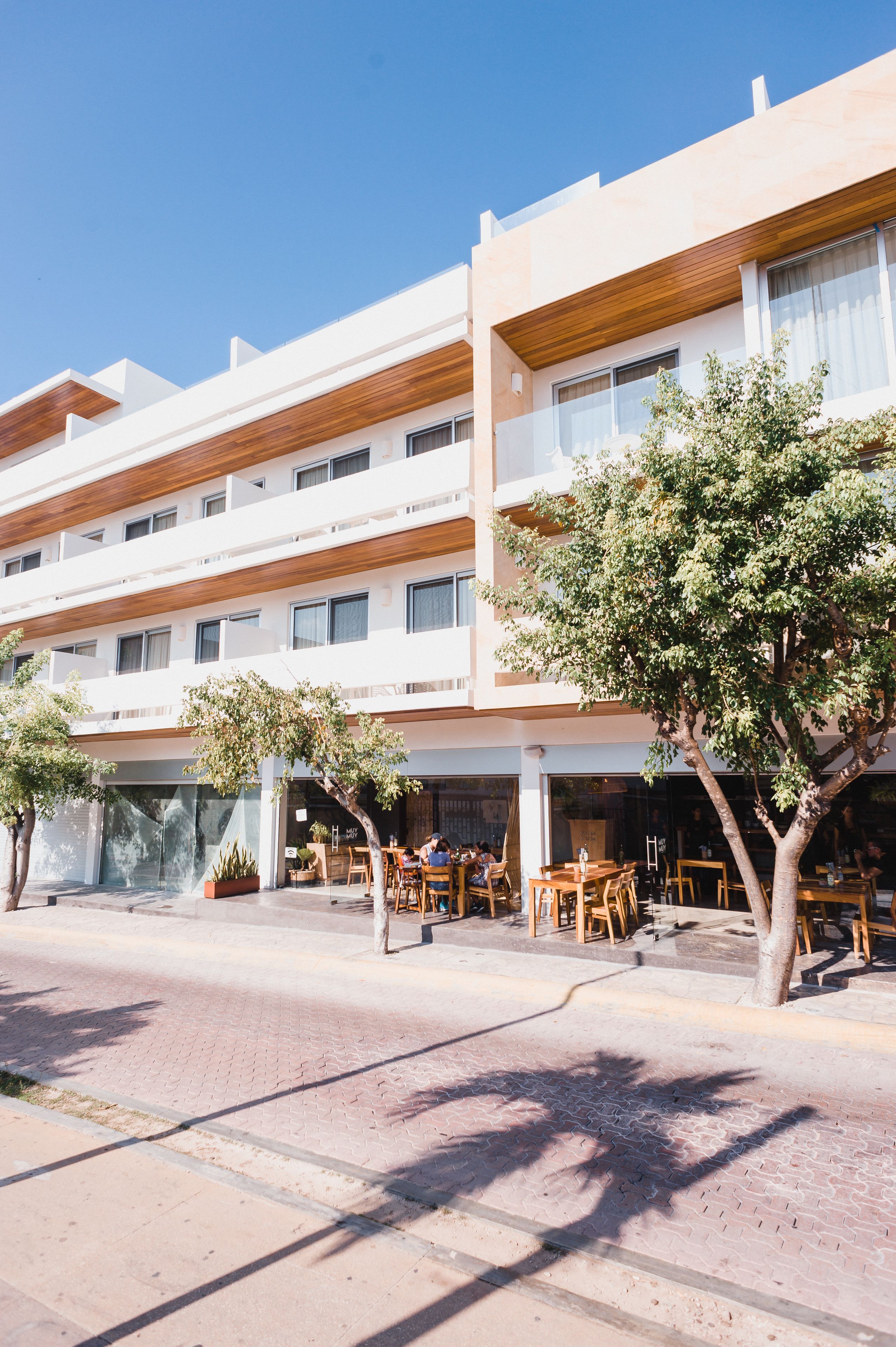 A multi-story hotel with outdoor seating and a tree in the foreground.