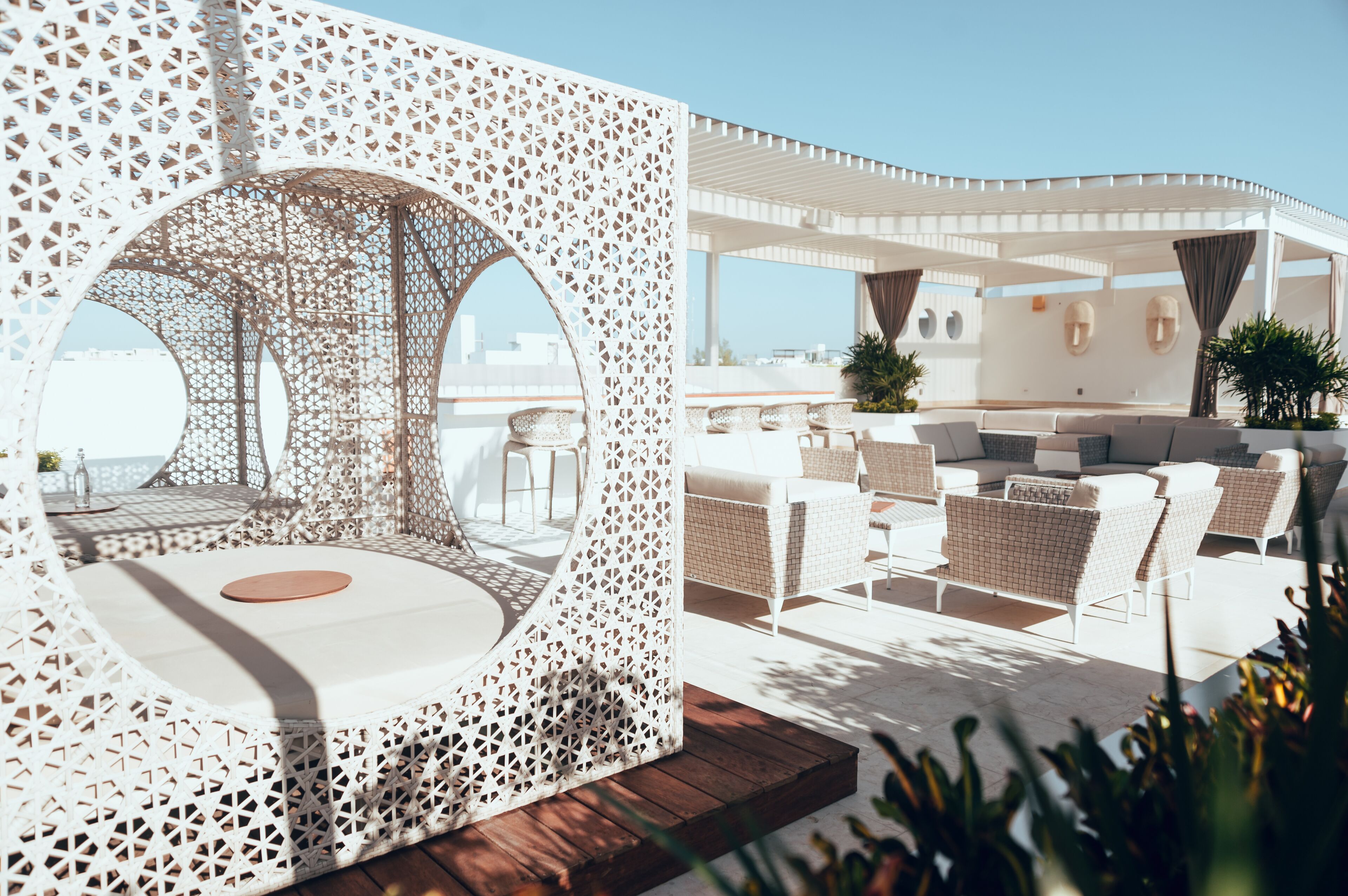 Un salón en la azotea con una zona de estar circular, mobiliario de mimbre blanco y vistas del horizonte de la ciudad.