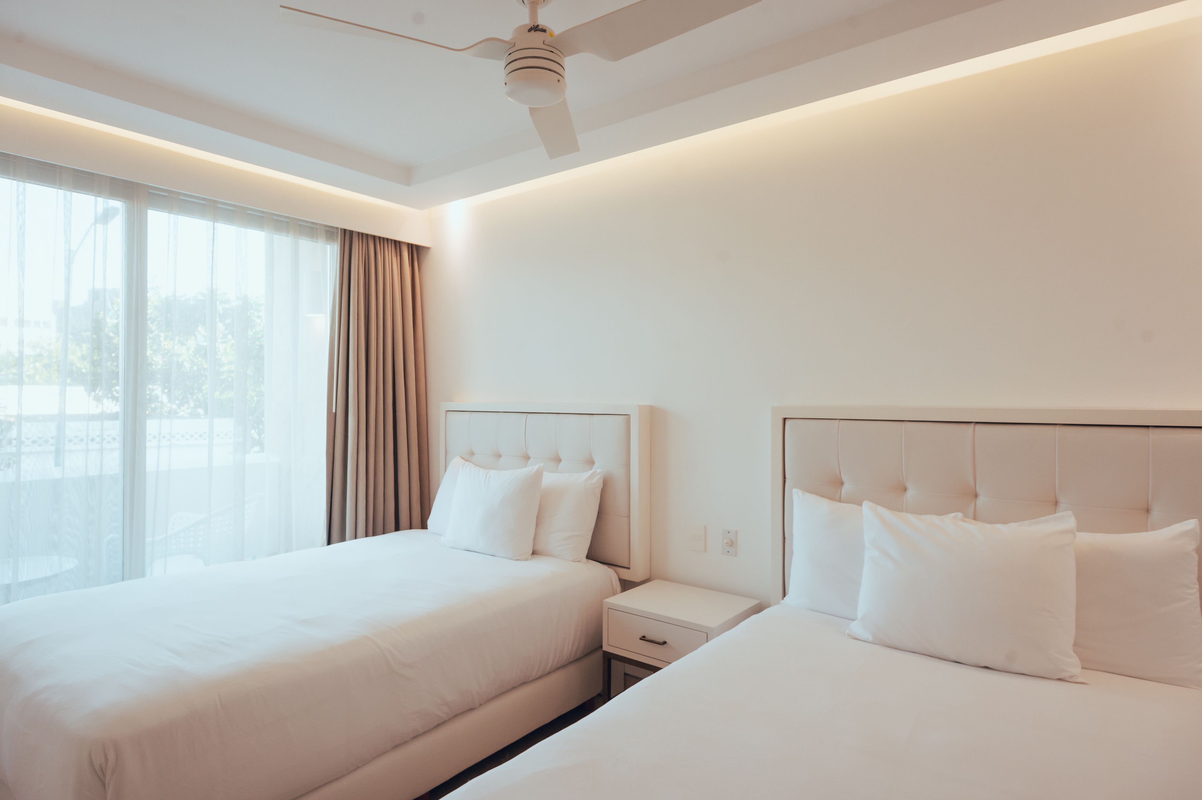 A hotel room with two beds, a ceiling fan, and a large window with curtains.