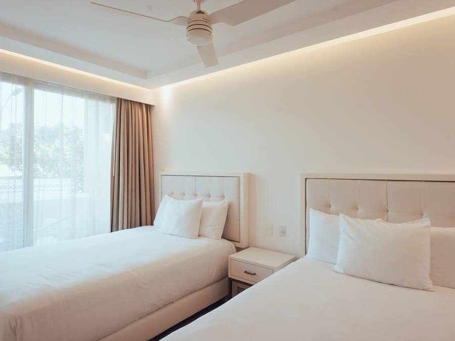 A hotel room with two beds, a ceiling fan, and a large window with curtains.
