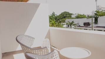 Een balkon met witte rieten stoelen en een kleine ronde tafel, met uitzicht op een stadslandschap met groen en gebouwen.