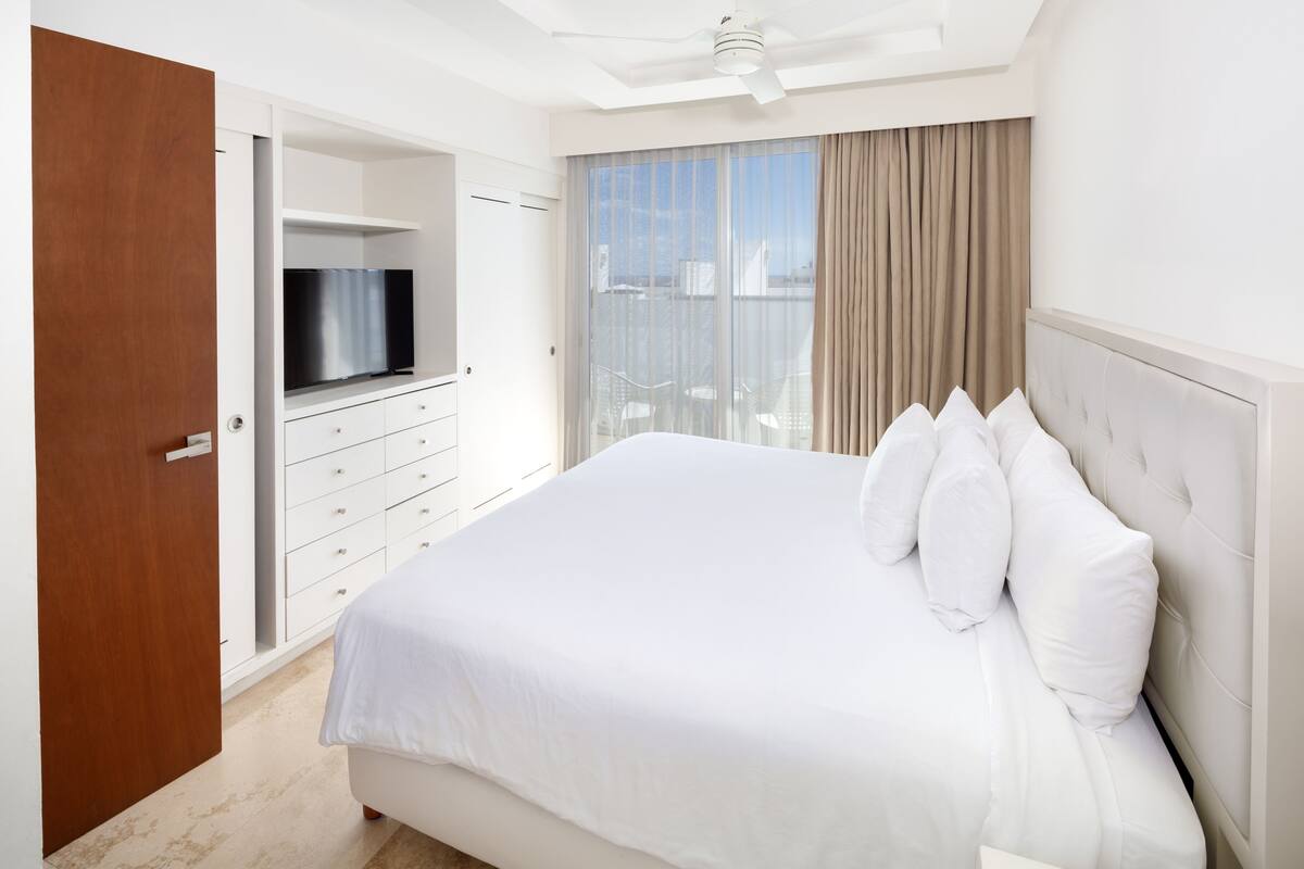 A hotel room with a large bed, a television on a stand, a wardrobe, and a balcony with a view.