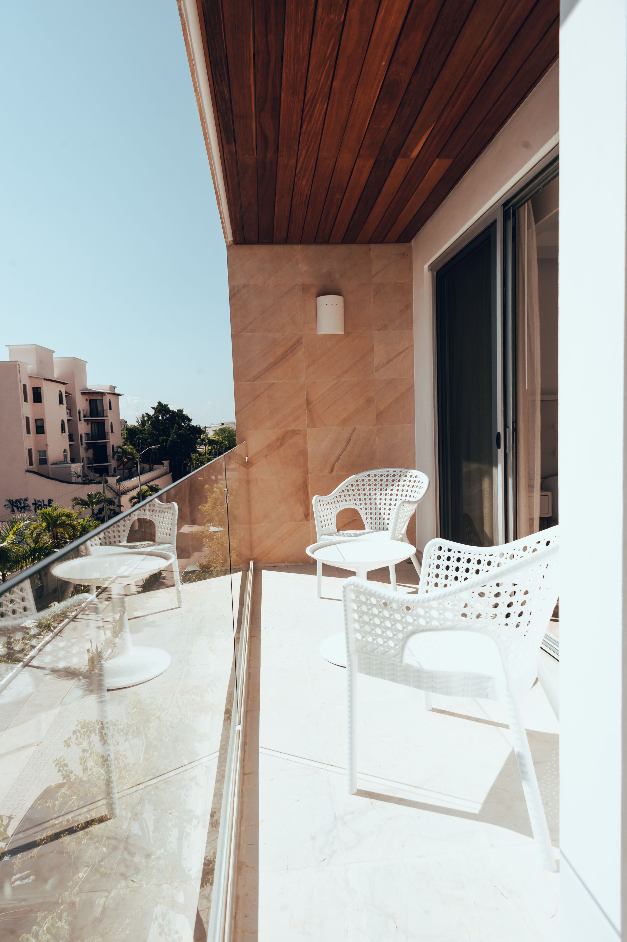 Ein Balkon mit weißen Korbstühlen, einem kleinen runden Tisch und einem Glasgeländer.