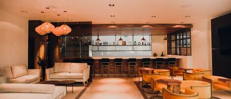 A modern lounge area with sofas and chairs, a bar with shelves, and pendant lighting.