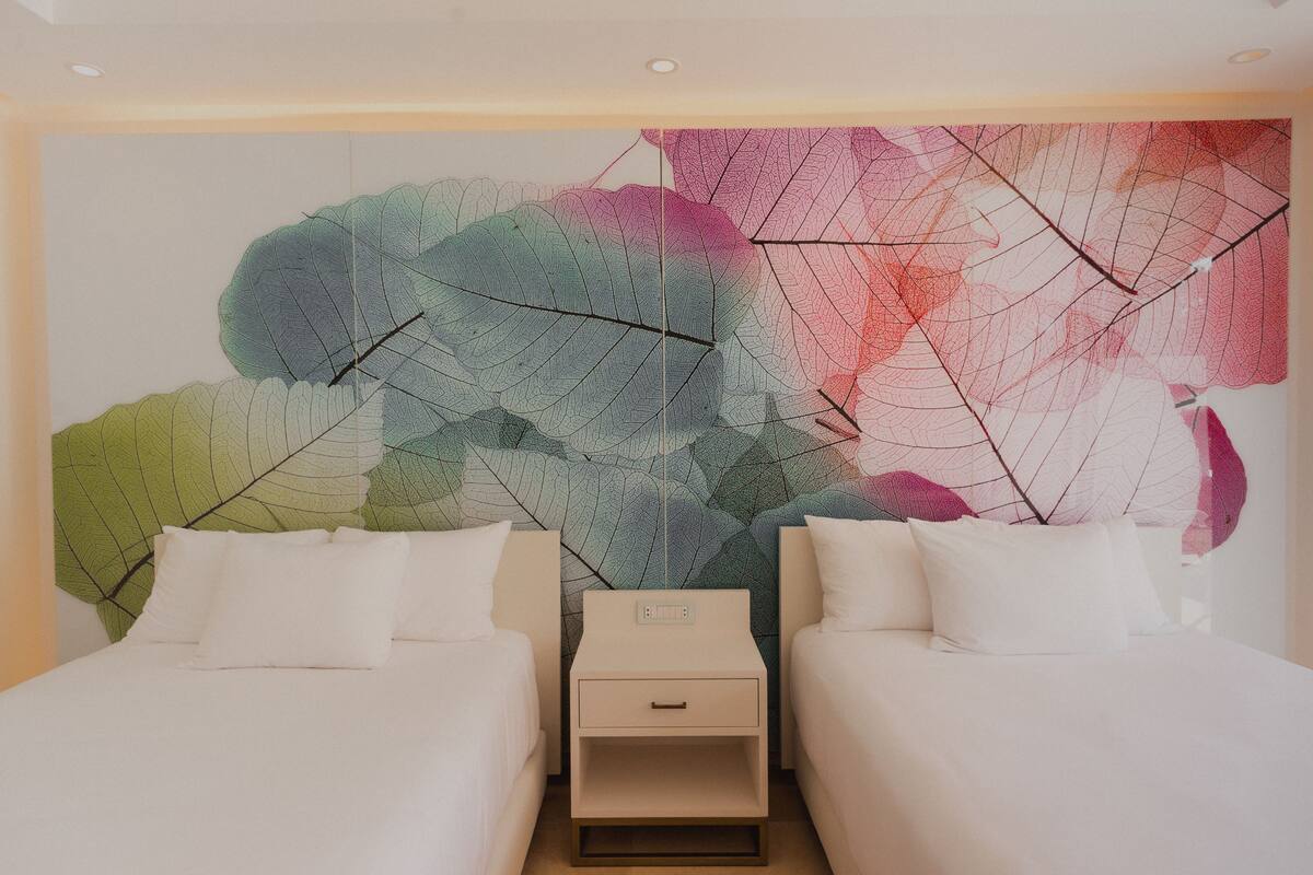 A hotel room with two beds, a nightstand, and a large abstract wall art piece.