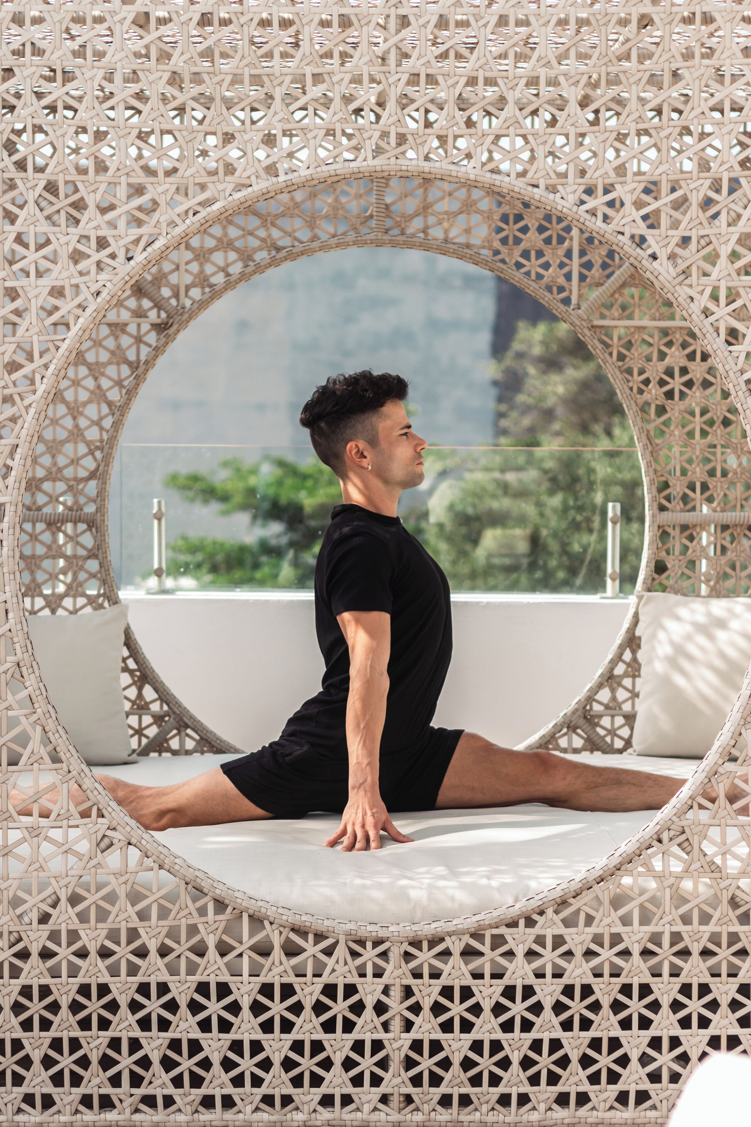 A person performing a split in a room with a circular mirror and a view of greenery outside.