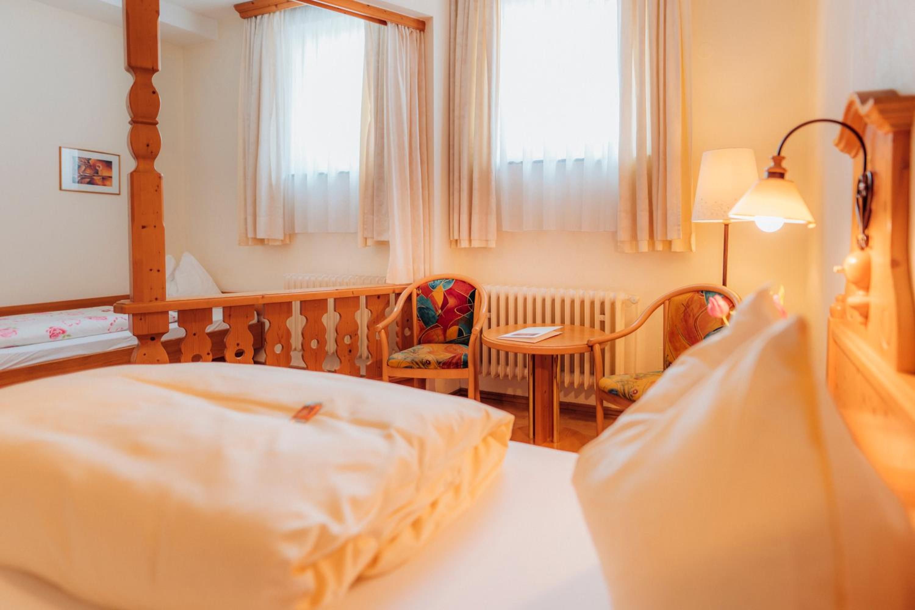 Una habitación de hotel con cama, una silla, una mesa, una lámpara y una ventana con cortinas.