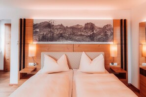 A double bed with a headboard, two bedside tables, and a wall-mounted artwork depicting a mountainous landscape.