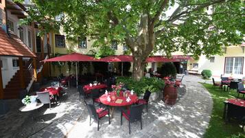 An outdoor dining area with tables and chairs, covered by red umbrellas, and surrounded by trees.