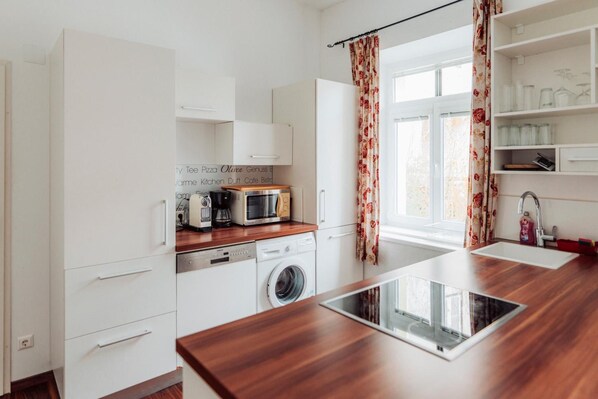 A modern kitchen with white cabinets, a wooden countertop, a washing machine, a microwave, and a window with floral curtains.
