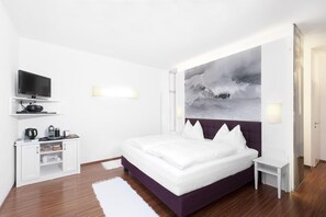 A hotel room with a bed, a flat-screen TV, a coffee machine, and a painting on the wall.