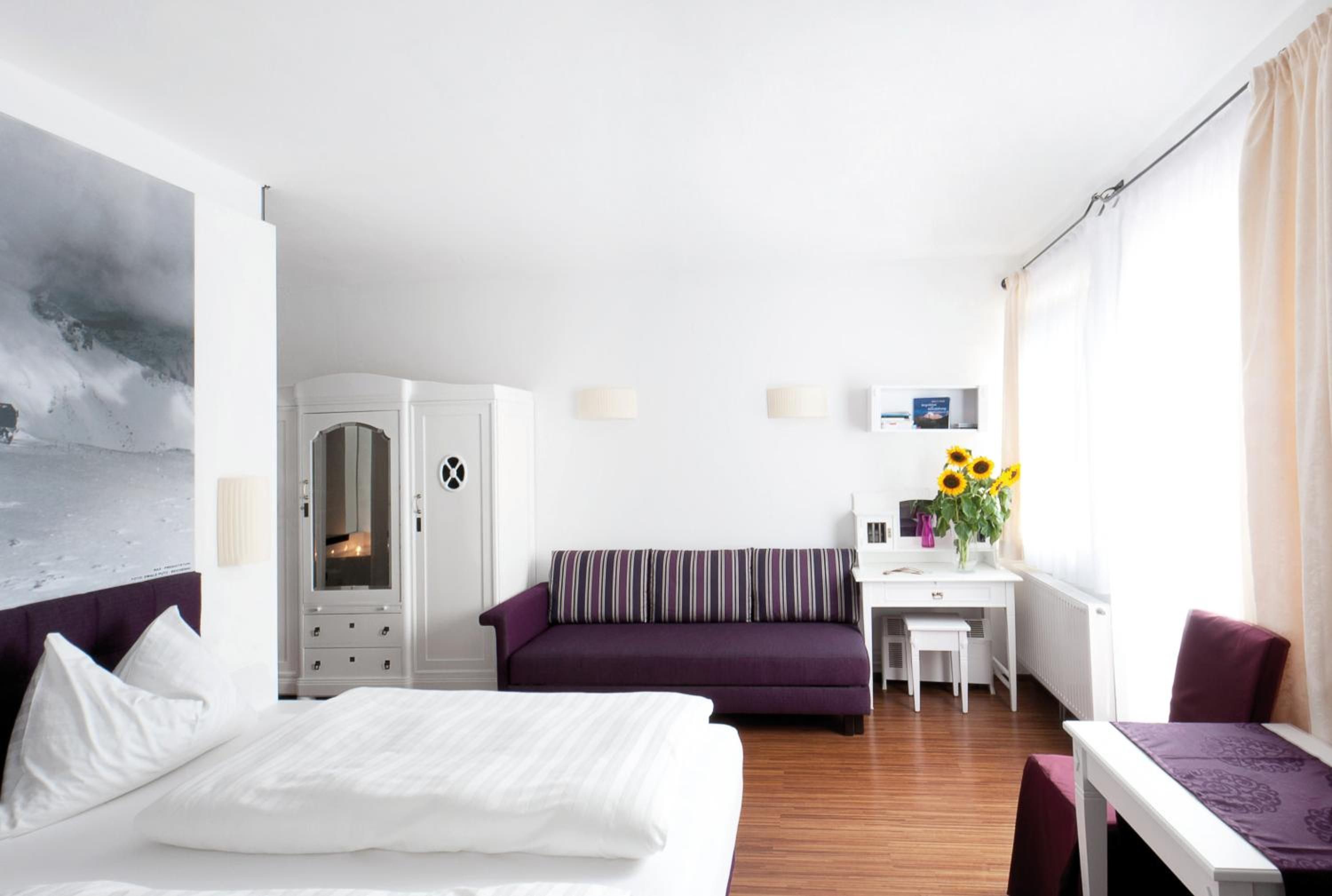Ein Hotelzimmer mit einem Bett, einem violetten Sofa, einem Schreibtisch und einem Fenster mit Vorhängen.
